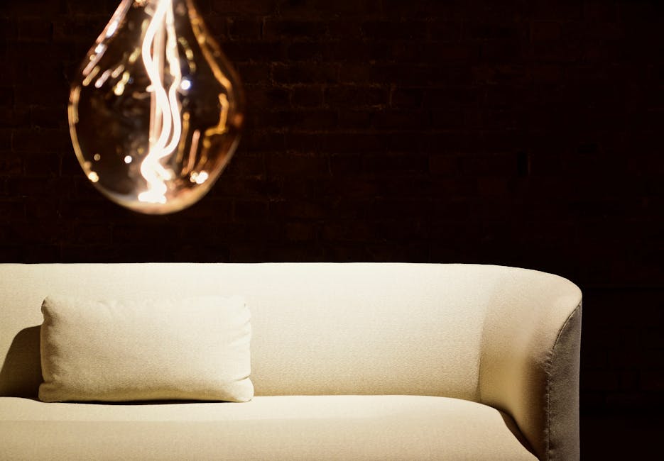 A contemporary interior featuring a glowing light bulb and a stylish beige sofa against a dark backdrop.